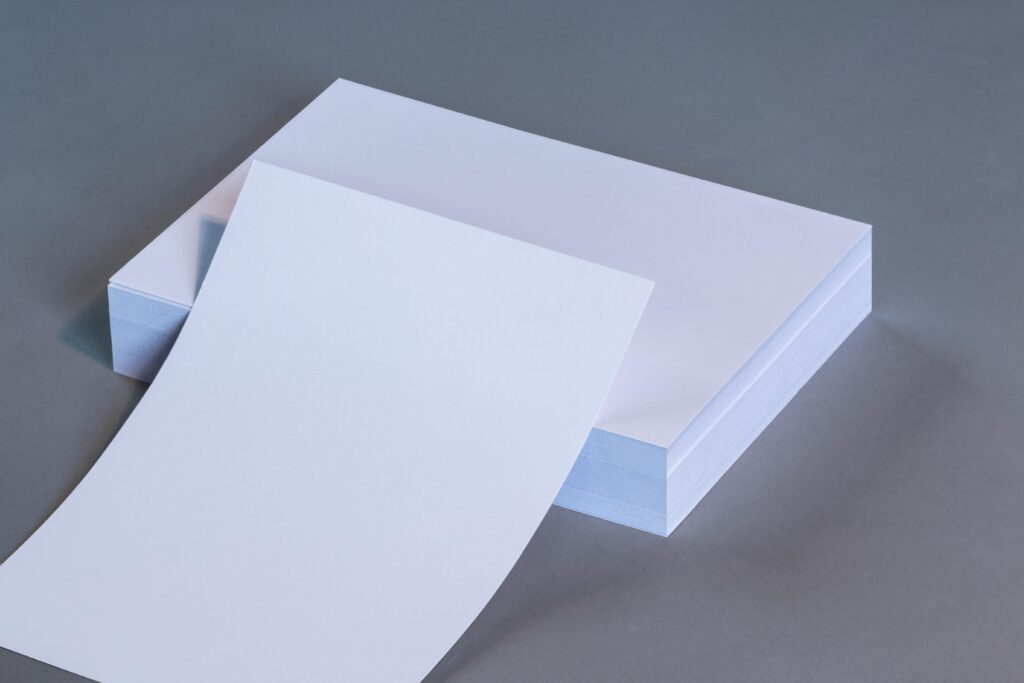 A high-quality image showing blank white paper sheets stacked on a neutral gray surface.